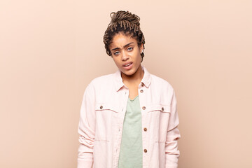 young afro woman feeling puzzled and confused, with a dumb, stunned expression looking at something...