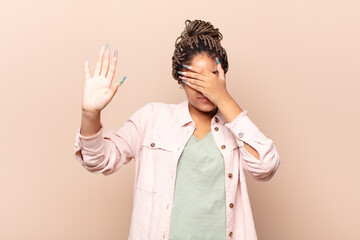 young afro woman covering face with hand and putting other hand up front to stop camera, refusing...