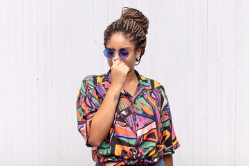 young afro woman feeling disgusted, holding nose to avoid smelling a foul and unpleasant stench