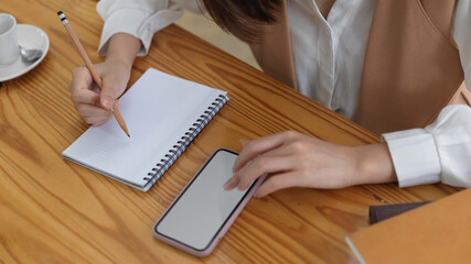 Female looking informations on mock up smartphone and write it down in blank notebook