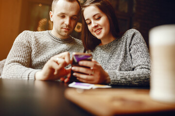 Cute couple sitting in a cafe. Pair in a gray sweaters. Man with mobile phone. Woman drink coffee
