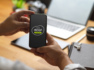 Male hand holding mock up smartphone while sitting at office desk