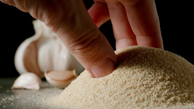 Male hand taking a pinch of white garlic grains by a pile