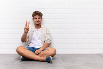 young man smiling and looking friendly, showing number three or third with hand forward, counting...