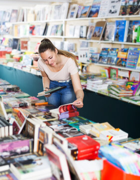 Portrait of positive young woman choosing textbooks in book shop..