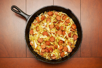 A cast iron skillet with fried cabbage and kielbasa sitting on a wood table.