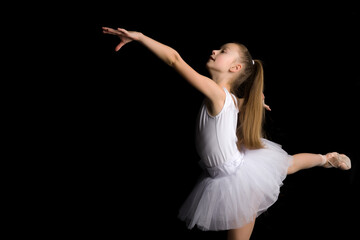 Cute little girl in a tutu and pointe shoes is dancing in the studio on a black background.