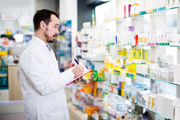 Young male pharmacist checking assortment of drugs in drugstore