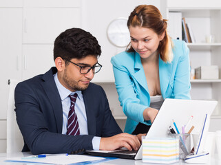 Businessman and businesswoman sitting at desk and working together at office