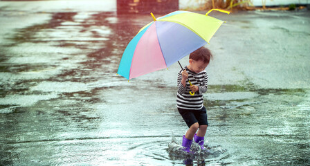 Little young human held a colorful umbrella playing in the rain happily on a rainy day.