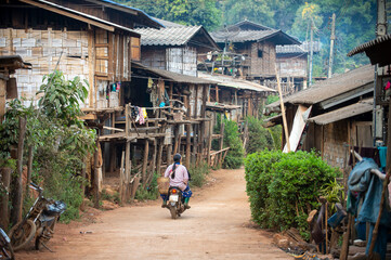 A small rural village, a hill tribe village in Chiang Mai Thailand, houses made of wood and bamboo, and a dirt road with a motorbike.