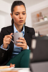 Portret of business woman watching on tablet and drinking a cup of coffee. Freelancer reading the last news online before going to work, using modern technology in the kitchen while eating a healthy