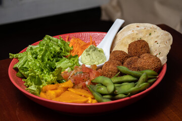 Vegan falafel with vegetables and tzatziki sauce. Arabic food. Middle eastern style Buddha bowl with falafel, pita, tomato, soybean, butternut squash, greens, salad, and tahini sauce. Orange, green