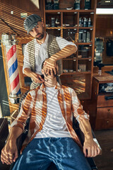 Professional hair-cutter turning head of his client ot the side to shave him