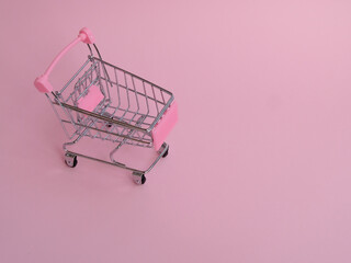 Small shopping cart with big cucumber on pink background