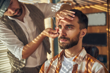 Calm young client of a barbershop sitting motionless during a shave