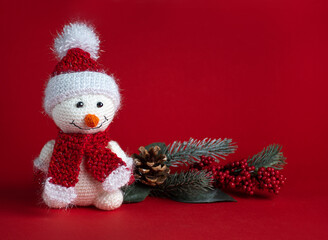 A snowman in a Santa Claus hat stands next to the branches of a Christmas tree on a red background: happy New year, place for text