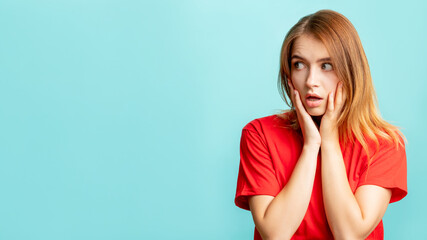 Overwhelmed woman. Disturbing information. Portrait of confused lady in red with hands on face looking scared at copy space isolated on blue background. Unbelievable news.