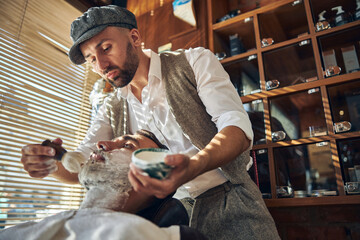 Careful hair-stylist applying shaving cream on his customer