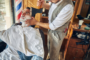 Hairdresser operating an axe while shaving his customer