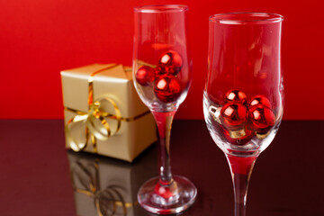 Two champagne glasses with small Christmas balls inside against red background