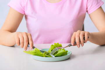 Woman eating salad at table, closeup. Concept of anorexia