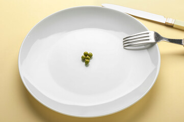 Plate with peas and cutlery on color background. Concept of anorexia