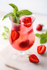 Glass of fresh strawberry mojito on light background