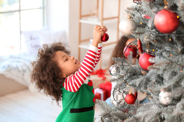 Cute African-American girl decorating Christmas tree at home