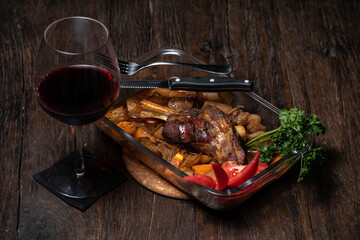 Roasted lamb leg with potatoes fresh cooked out of the oven. Delicious roasted ribs. Appetizing baked lamb shins from oven with vegetable garnish of french fries, parsley. Red wine. Dark wood table