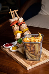 Meat beef shish kebab with vegetables and spices with barbecue sauce and ketchup, mustard on a dark background on a wooden cutting board. Shish kebab BBQ meat. Fish kebab with bell pepper. French fry