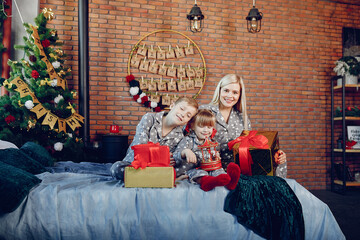 Beautiful mother in a gray pajamas. Family sitting on a bed. Little girl and boy near christmas tree