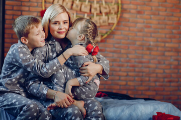 Beautiful mother in a gray pajamas. Family sitting on a bed. Little girl and boy near christmas tree