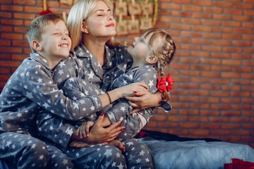 Beautiful mother in a gray pajamas. Family sitting on a bed. Little girl and boy near christmas tree