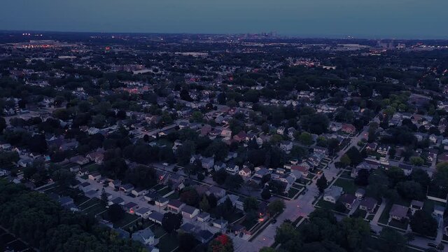 Aerial drone view of American suburban neighborhood at night time. Establishing shot of America's  suburb. Residential houses in the foreground, skyscrapers in the downtown in the background  