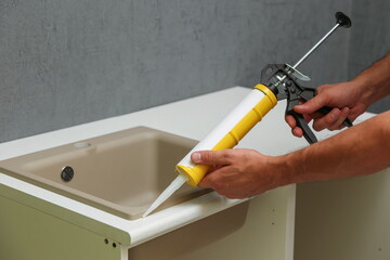 worker seals kitchen sink with sealant. hands of worker works with construction sealant gun in the kitchen. 