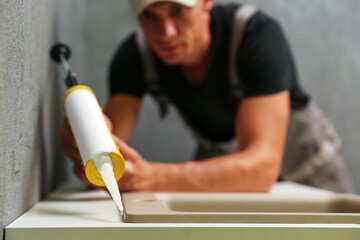 Fototapeta na wymiar worker seals kitchen sink with sealant. hands of worker works with construction sealant gun in the kitchen. 