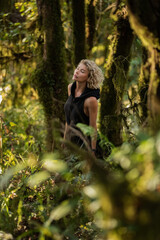  Brooding dreamy young girl blonde, black dress with a hood standing by a tree. The girl got lost in the woods. Trekking, fantasy, magical mystical forest. Girl standing by a tree. High quality photo