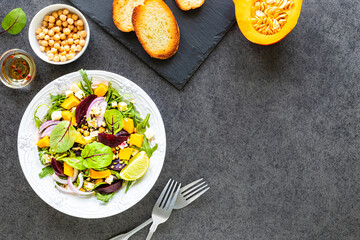 Fresh vegetable salad with beets, arugula, red onions, sorrel, chickpeas, pumpkin in a white plate on a black background. Top view