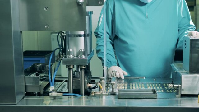 Man works at medical laboratory, checking capsules. Pharmaceutical factory production line.