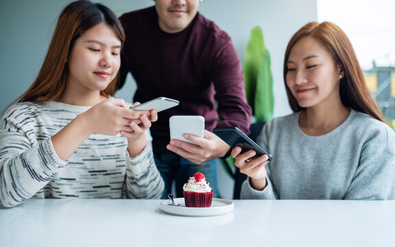 Group of young people using mobile phone to take a photo of a cupcake before eat in cafe
