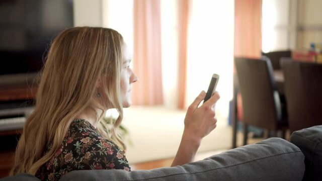 Woman sitting in living room scrolls on smart phone, gets angry and throws phone