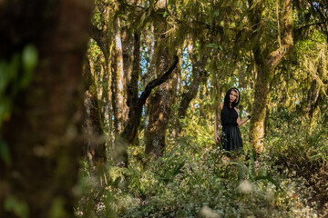 Girl in a black hood dress walking through the woods, enjoying the walk fashion. Anxious tired, worth, brooding, dreamy in green forest, trees, path. Enjoying the walk. Magic. High quality photo