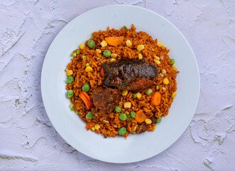 Jollof Rice and vegetables with stewed Goat meat in a white ceramic plate on an embossed background