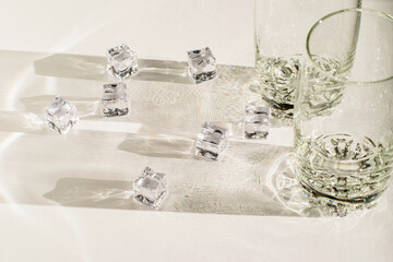 Transparent glasses and pieces of ice on the white background, sunlight and long hard shadows.