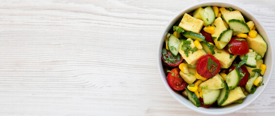 Fresh Avocado Tomato Salad in a bowl on a white wooden background, top view. Flat lay, overhead, from above. Copy space.
