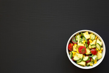 Fresh Avocado Tomato Salad in a bowl on a black background, top view. Flat lay, overhead, from above. Space for text.