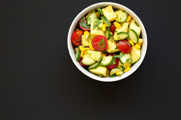 Fresh Avocado Tomato Salad in a bowl on a black surface, top view. Flat lay, overhead, from above. Copy space.