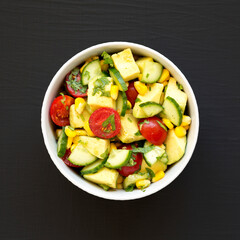 Fresh Avocado Tomato Salad in a bowl on a black background, top view. Flat lay, overhead, from above.