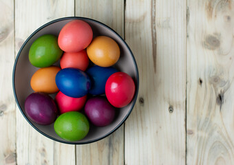 colored eggs in a bowl on a wooden background and negative space